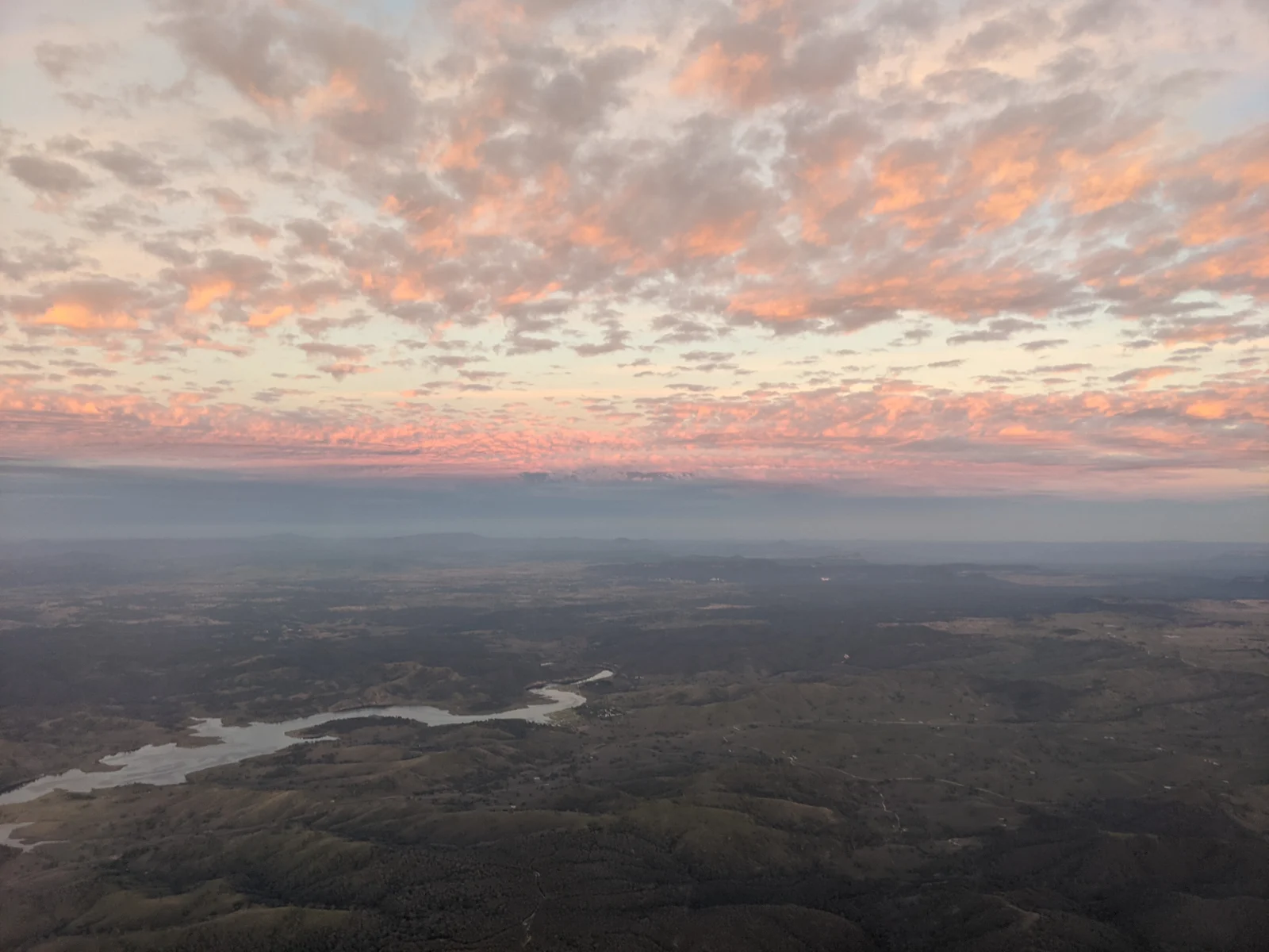 Aerial view of rolling hills and a winding body of water beneath pink and grey clouds
